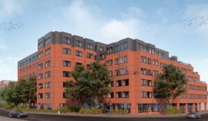 A modern commercial building with a red brick exterior and flat roof converted into functional space, surrounded by trees, on a sunny day.